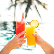 Hands raising a toast with tropical drinks